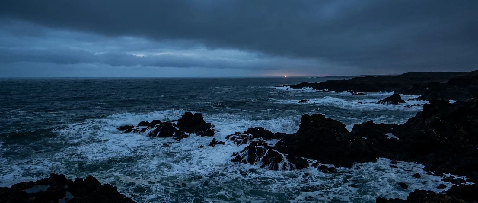 A dark, churning storm sea at dusk with black rocks and white foam, a faint distant light on the horizon